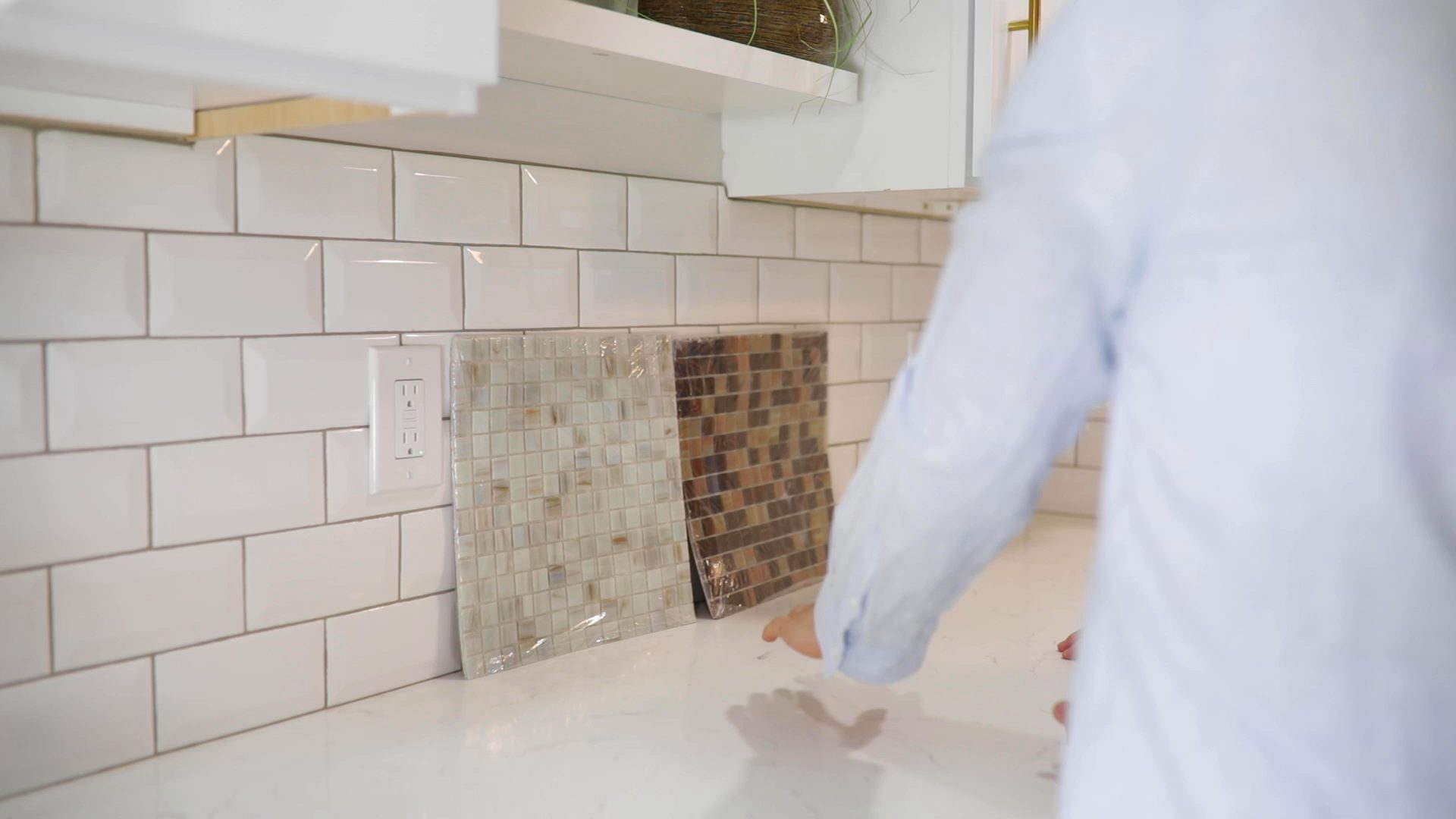 A homeowner comparing tile samples against a white subway tile kitchen backsplash