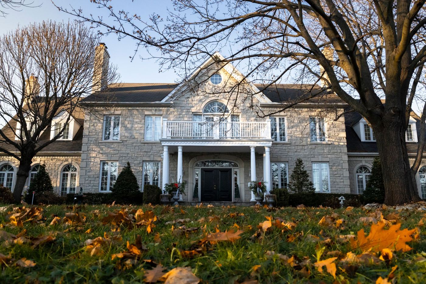 An established home under mature trees at the turn of the season, leaves down on the lawn