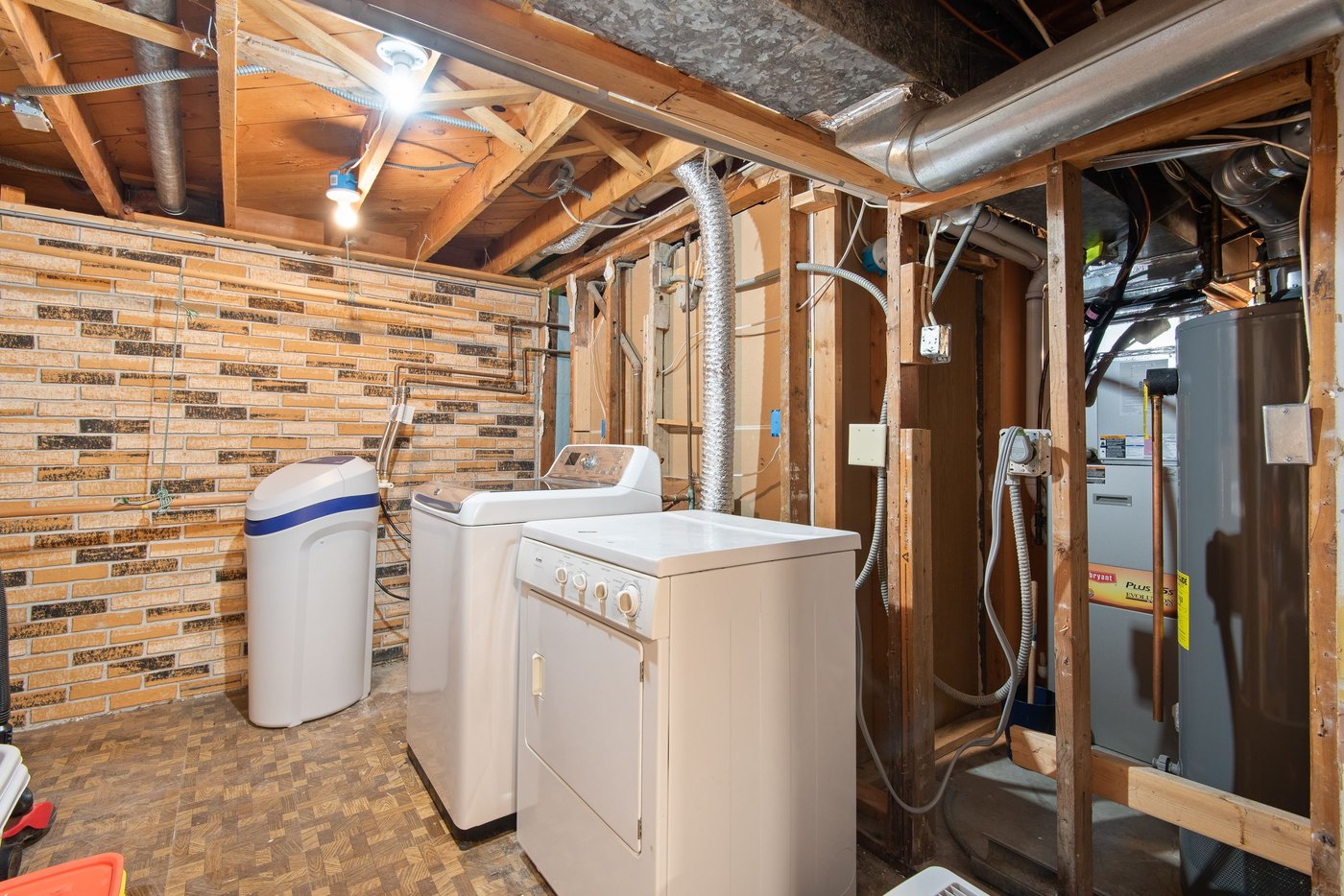 A sump pit with a submersible pump and discharge pipe in the corner of a clean unfinished basement